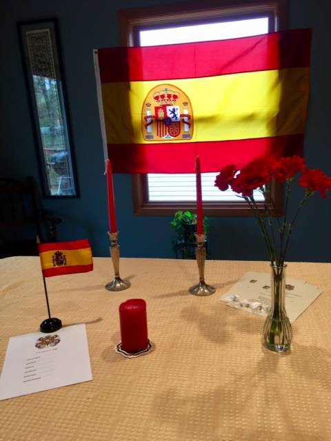 Sigma Delta Pi flag hung up in background with red candles and a vase of red carnations on a table in the foreground
